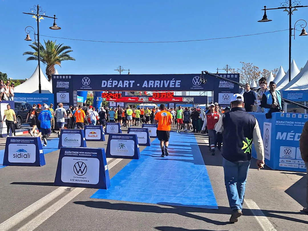 Runners crossing finish line at sunny Marrakesh Marathon event.