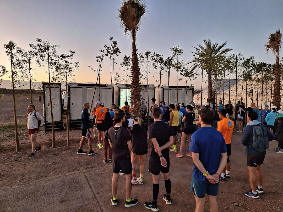 Runners gather at dawn near palm trees and portable restrooms.
